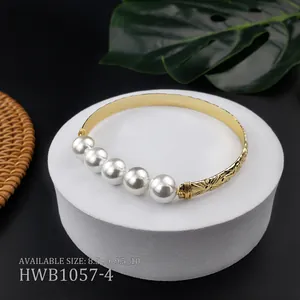 Dettaglio del bracciale in rame dorato inciso con fiori e cinque grandi perle bianche