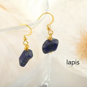 Close-up of gold hook earrings with raw lapis lazuli stones on a glass edge