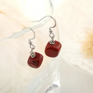 Detail shot of natural red jasper cube drop earrings hanging on a glass with feathers