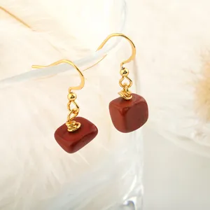 Detail of red jasper stone drop earrings with gold hooks hanging on glass rim