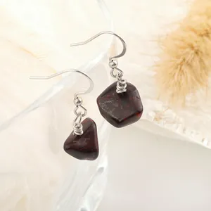 Macro shot of natural red jasper stone earrings with silver hooks on a glass rim