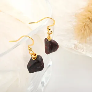 Macro shot of gold hook earrings with natural dark red raw stone pendants on glass