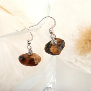 Close-up of natural stone drop earrings with silver hooks on a glass edge with feathers