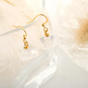 Detail of natural crystal earrings with gold hooks hanging on glass with soft feather decor