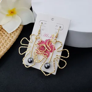 Golden monstera leaf outline earrings with dark pearl drop on Aloha card packaging