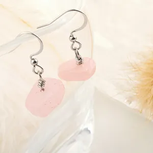 Macro detail of natural pink crystal hook earrings hanging on a transparent glass edge