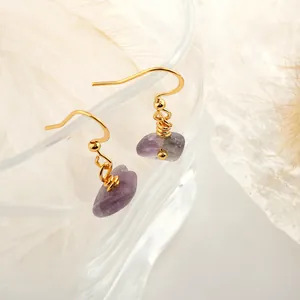 Close-up of handmade gold earrings with raw purple amethyst crystals on a glass edge