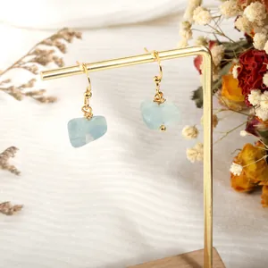 Detail of light blue raw stone earrings with gold hooks on a wooden display stand