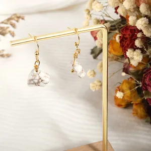 Detail of bohemian natural white stone earrings with gold wire wrap on a display stand