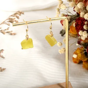 Detailed shot of yellow crystal drop earrings hanging on a gold display stand