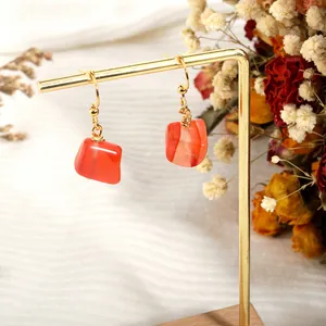 Detail of natural orange carnelian stone earrings hanging on a golden display stand