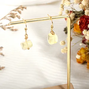 Close-up of gold cubic crystal earrings hanging on a minimalist display stand