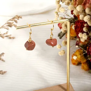 Detail of bohemian gold hook earrings with natural red goldstone on a display stand