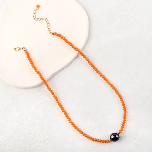 Close-up of orange faceted beads necklace with iridescent black pearl and gold clasp