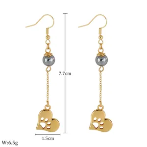 Detailed view of dangling gold earrings with grey pearl and heart paw print pendant