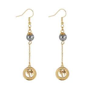 Detail of gold palm tree earrings with Hawaii engraving and grey pearl charms