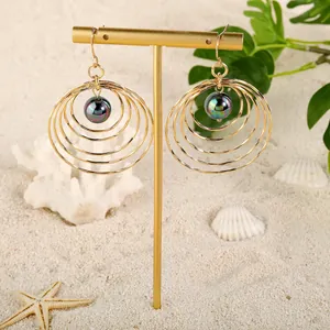Gold multi-layer hoop earrings with black shell pearl on beach sand summer backdrop