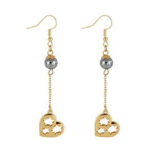 Detailed close-up of gold heart drop earrings with shell pearls and turtle cutout motifs