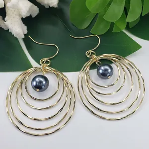 Macro view of multi-layer gold round earrings with dark grey pearl on tropical leaves
