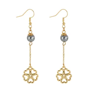 Macro detail of gold clover leaf drop earrings with grey pearl beads and fine chains