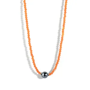 Macro view of orange beaded necklace featuring a large black pearl and gold spacers