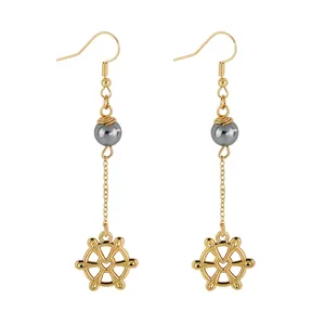 Detailed view of long gold earrings featuring grey pearls and heart steering wheel charms