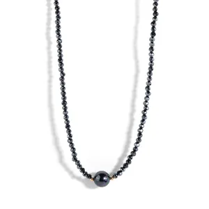Detail of dark beaded necklace featuring a large iridescent shell pearl and gold accents