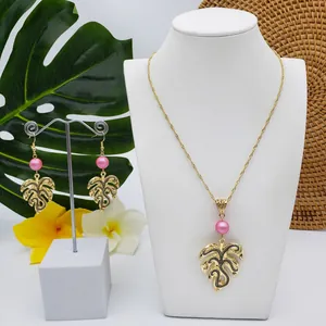 Detail view of gold tropical monstera leaf jewelry set with pink faux pearls on white bust