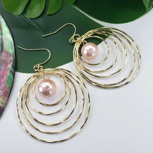 Macro detail of layered gold circular earrings featuring a central pink pearl pendant