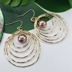Detail of layered gold hoop earrings featuring a central red faux pearl and hook closure