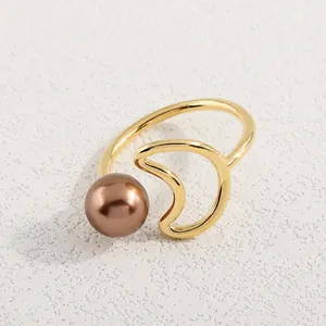 Detailaufnahme eines goldenen Rings mit Mondform und Bronzeperle auf strukturiertem Grund
