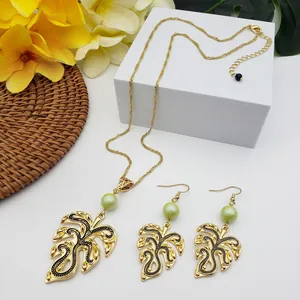 Detailed view of gold tropical monstera leaf jewelry set with green faux pearls