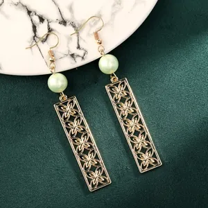 Detailed shot of gold镂空 clover earrings with light green pearls on marble surface