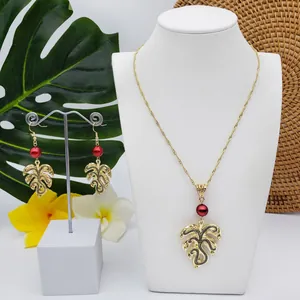 Detail of Monstera leaf pendant necklace and earrings with red pearl on display