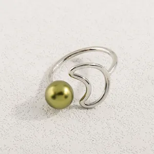 Detail eines verstellbaren Silbermondsrings mit olivgrüner Perle auf Texturhintergrund