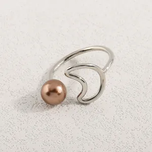 Detail eines silbernen offenen Rings mit Bronze-Perle und Wellendesign auf Stein