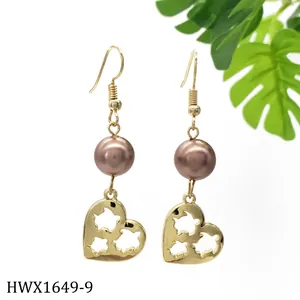 Detailansicht goldene Ohrhänger mit Herzanhängern und braunen Perlen auf weißem Hintergrund
