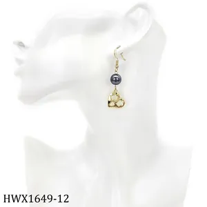 Detail eines Hängeohrrings mit Goldhaken, dunkler Perle und graviertem Herz-Bär-Anhänger