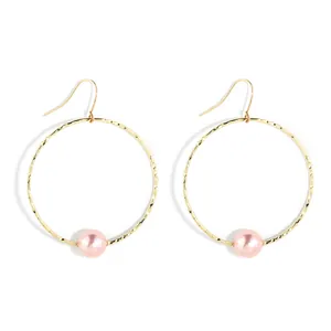 Close-up of golden hollow circle earrings featuring hammered texture and a pink pearl