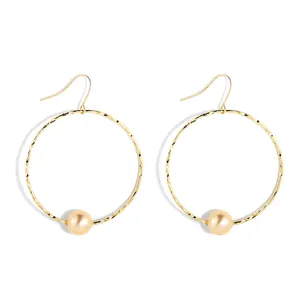 Detail of gold hollow hoop earrings featuring textured metal and large champagne pearls