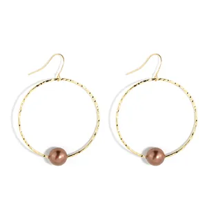 Detail of gold hammer-textured hoop earrings featuring a single brown mother-of-pearl bead
