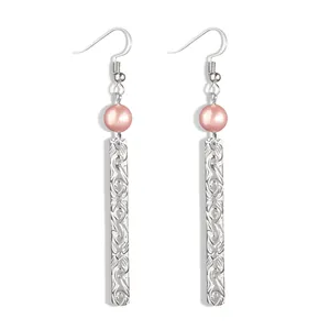Detailed close-up of long bar earrings with pink pearls and engraved floral metal patterns