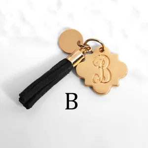 Macro view of gold flower charm with letter B engraving and black suede tassel keychain