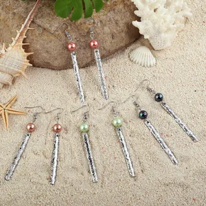 Hawaiian style long bar earrings with pearl charms and silver engraved metal on beach sand