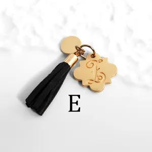 Detailed close-up of golden petal tag with engraved letter E and black suede tassel