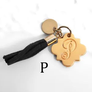 Close-up of golden flower pendant with letter P and black suede tassel on marble
