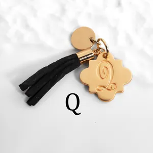 Detail of golden Q letter charm pendant with black suede tassel and sleek metal ring