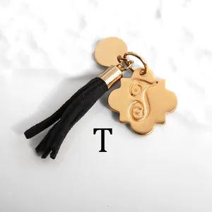 Detail of gold keychain with floral letter T pendant and black suede tassel on marble