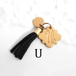 Detail of gold petal charm with engraved letter U and black leather tassel on marble