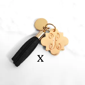 Detail of golden petal charm with letter X and black suede tassel on white marble